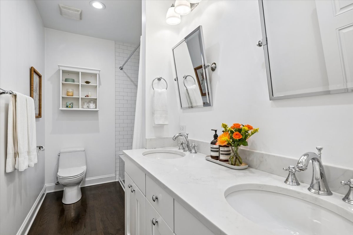 Bathroom with a long double-sink vanity, white cabinetry, and a subway-tile shower.