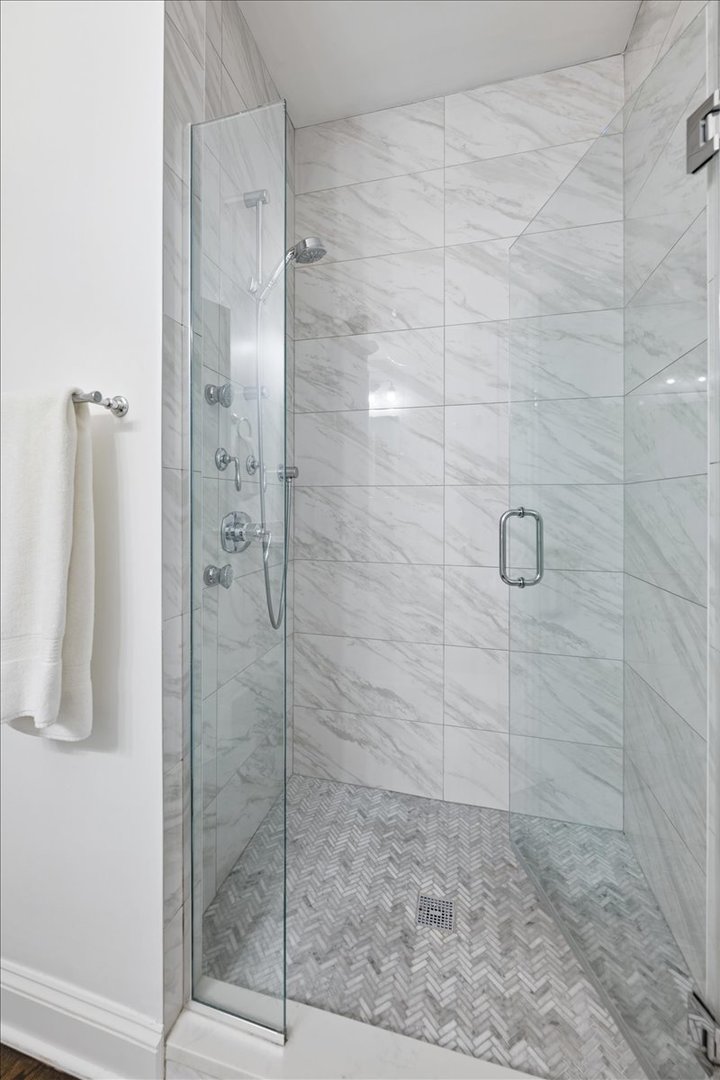 Walk-in shower with marble-look tile, a glass door, and a herringbone mosaic floor.