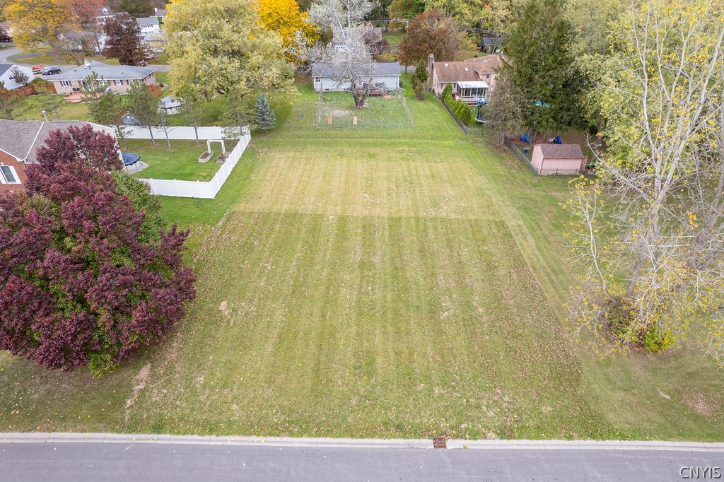 Aerial view of a broad, mowed lot bordered by neighboring homes and autumn trees.
