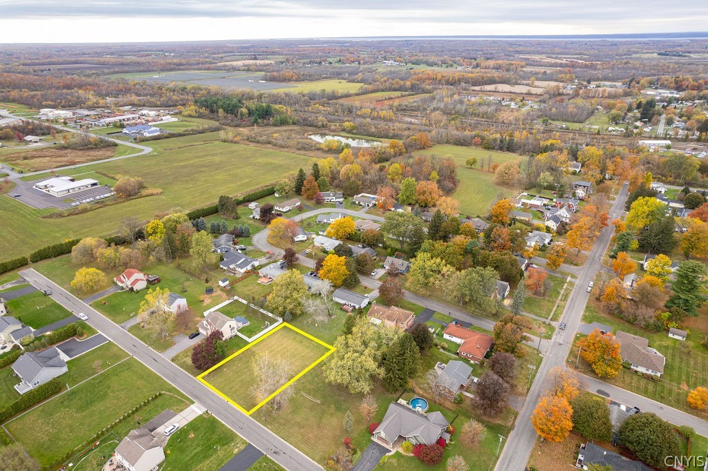 Aerial view of a vacant lot outlined in yellow among homes and autumn trees.