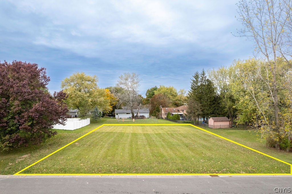 Vacant grassy lot outlined in yellow beside a street, with neighboring homes and autumn trees.