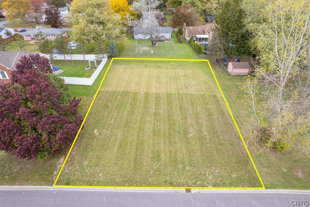 Aerial view of a vacant, street-front lot outlined in yellow among homes and autumn trees.