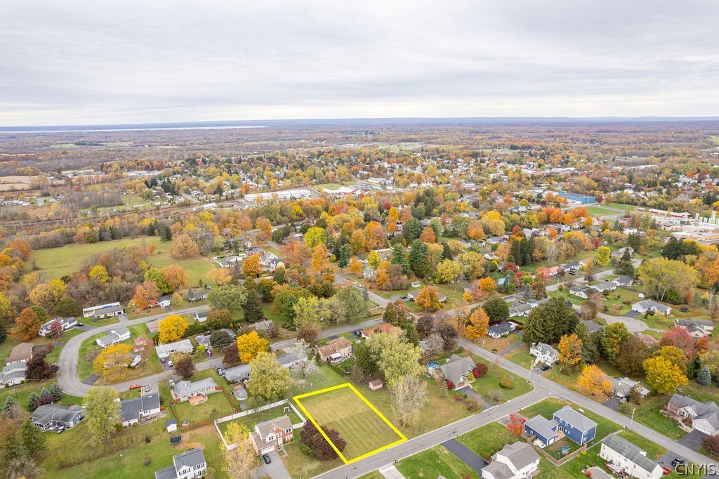 Aerial view of a vacant lot outlined in yellow beside a road in an autumn neighborhood.