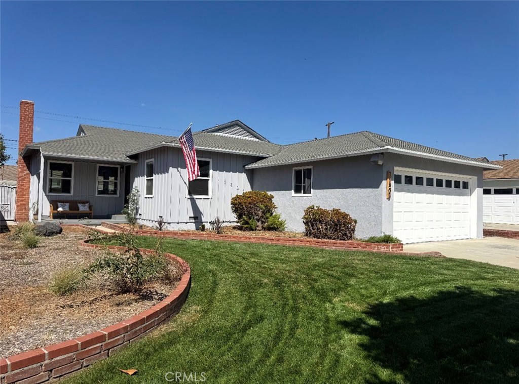 Gray single-story house with a white garage, American flag, and curved brick garden border.