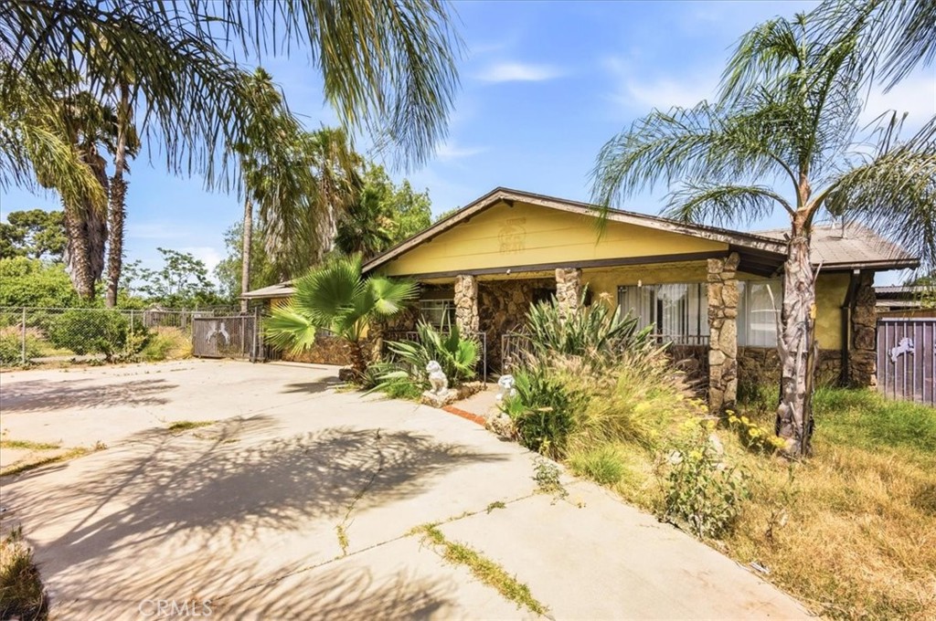 Single-story yellow home with stone accents, palm trees, and a wide concrete driveway.