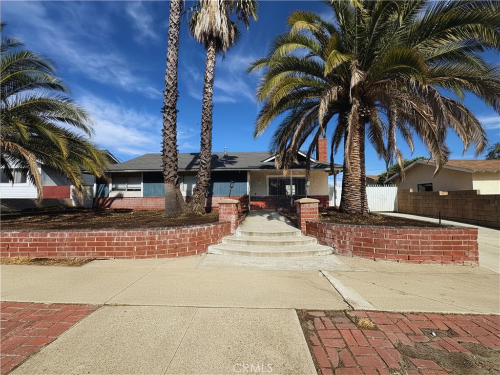 Single-story home with tall palm trees, brick planters, and curved front steps.