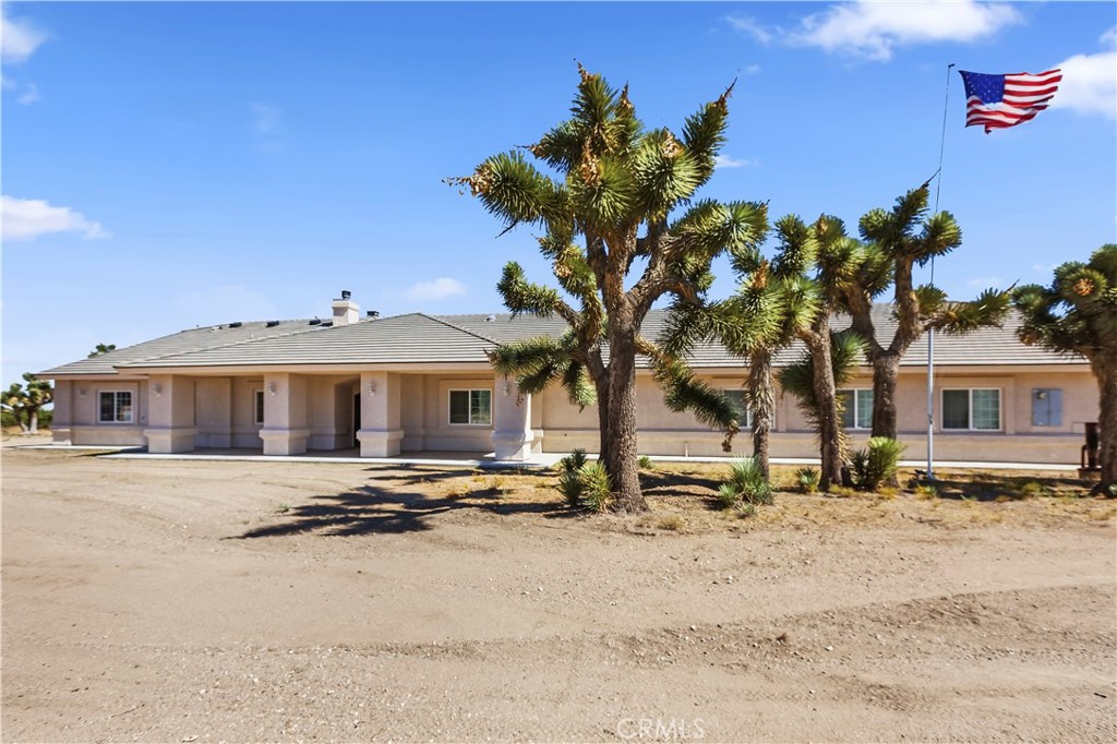 Single-story beige home with a tiled roof, Joshua trees, and an American flag in the front yard.