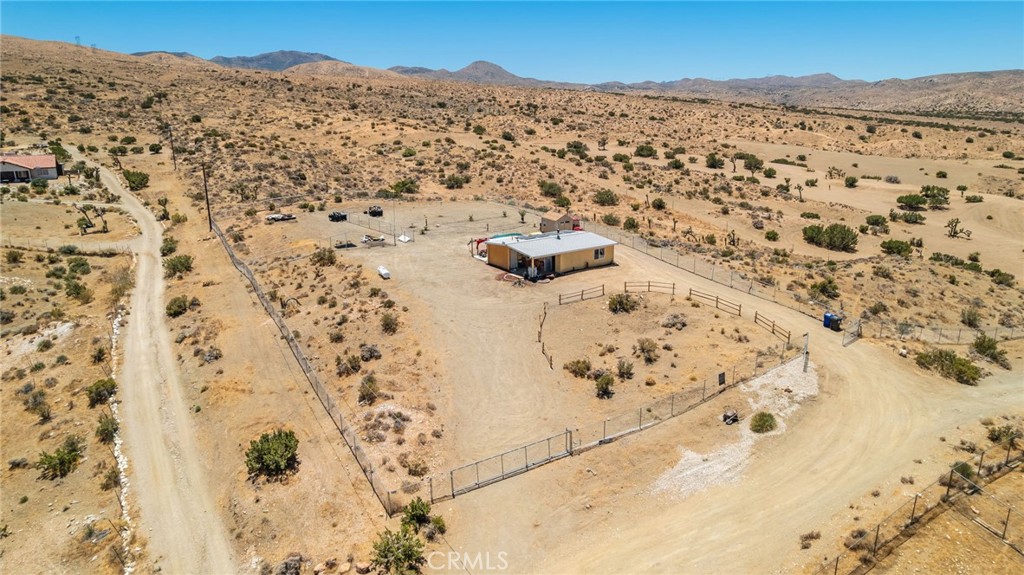 Aerial view of a fenced rural home and dry lot with mountains beyond.