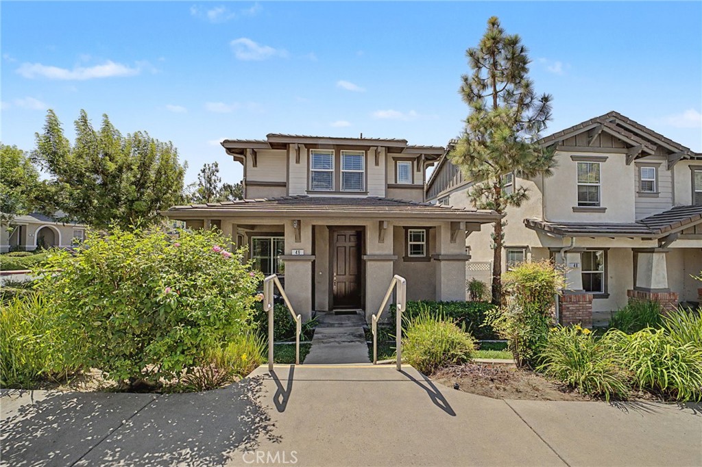 Two-story attached home with a front walkway, landscaped shrubs, and neighboring homes.