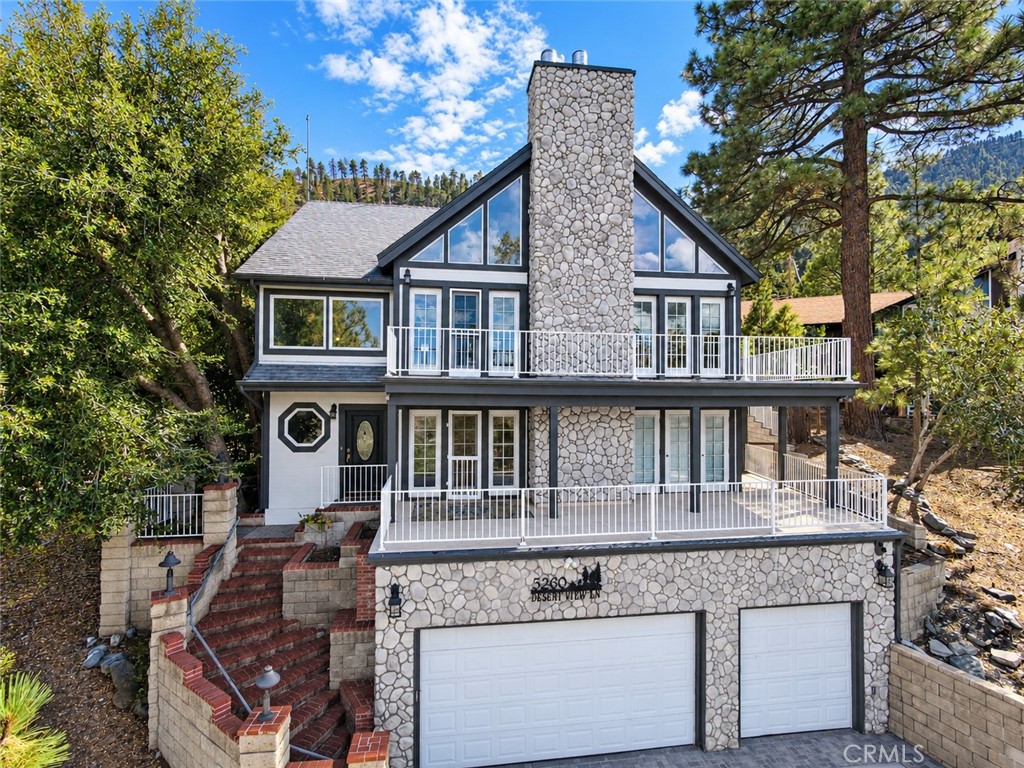 Stone-faced multi-level home with white-railed balconies, a prominent chimney, and a two-car garage.
