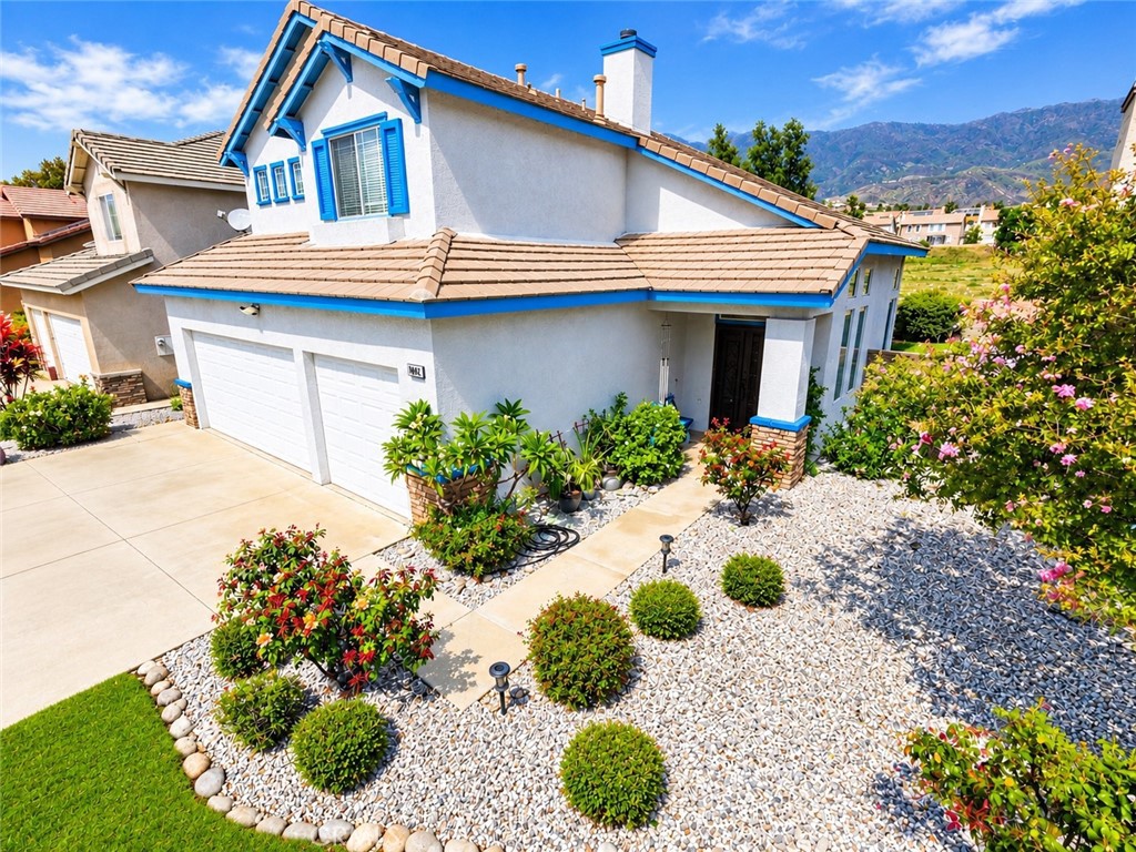 Two-story stucco home with blue trim, tile roof, attached garage, and landscaped rock garden.