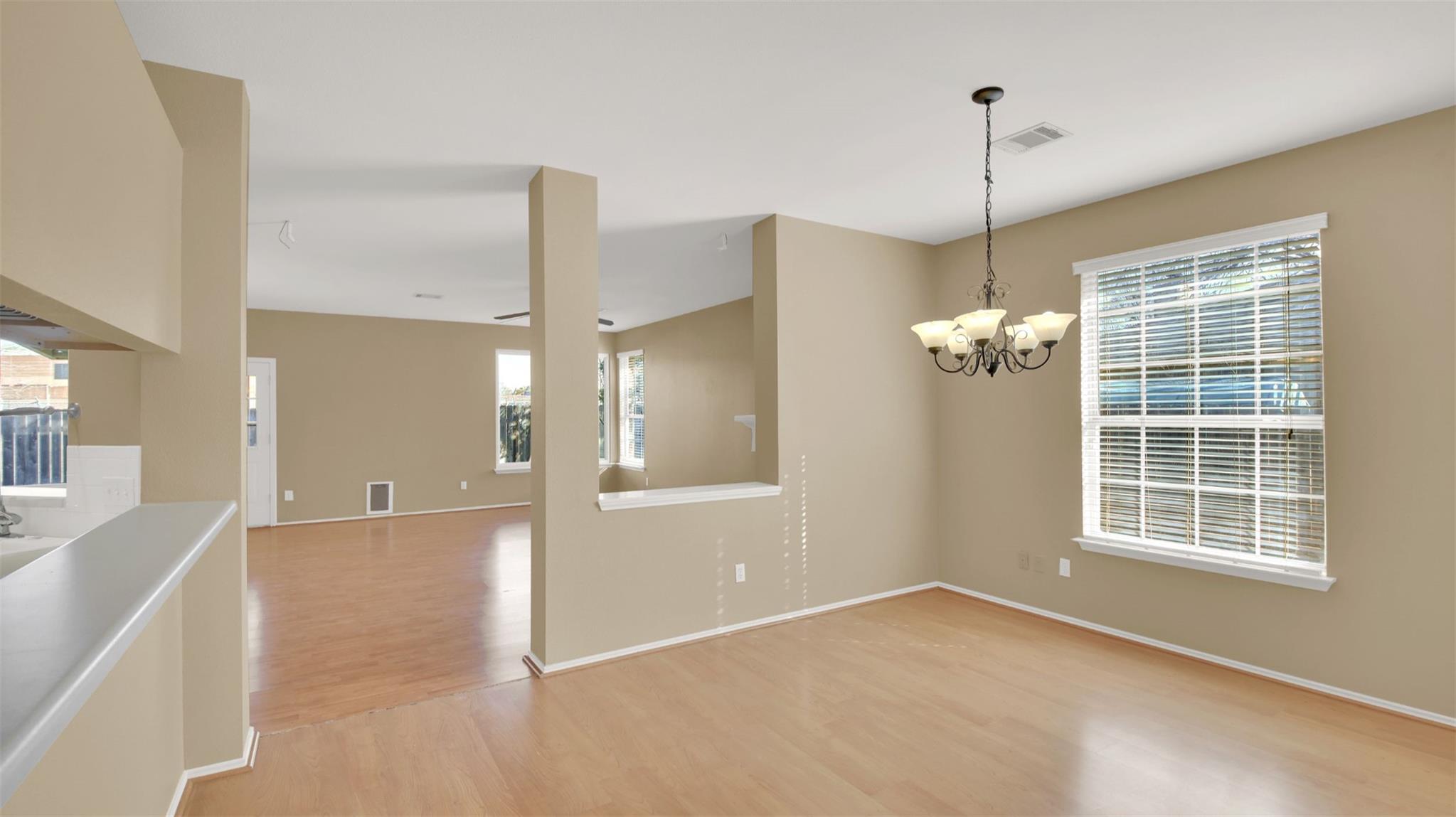 Vacant dining area with a chandelier, light wood floors, and a large window with blinds.