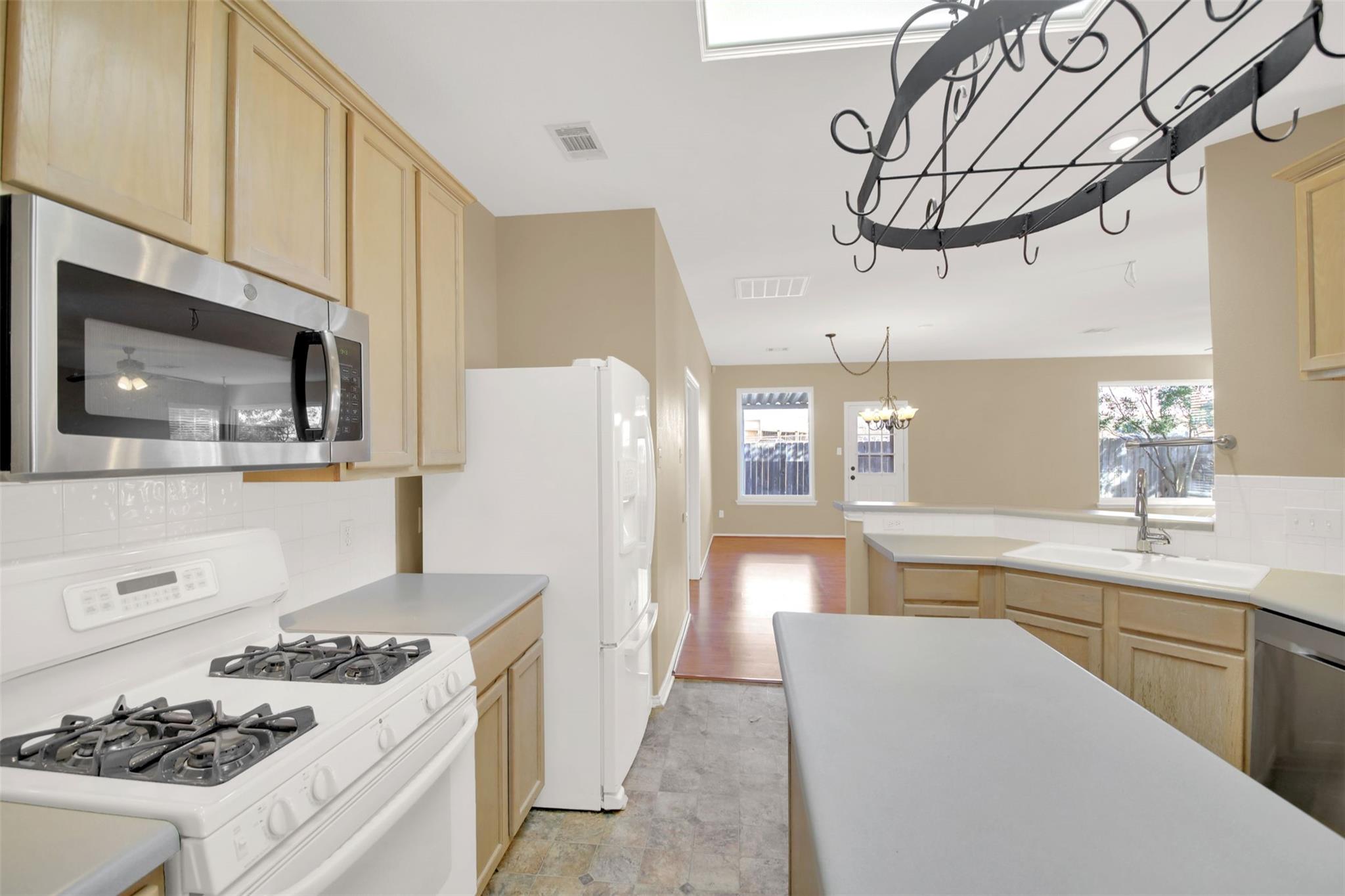 Kitchen with light wood cabinets, white appliances, a gray island, and a black hanging pot rack.