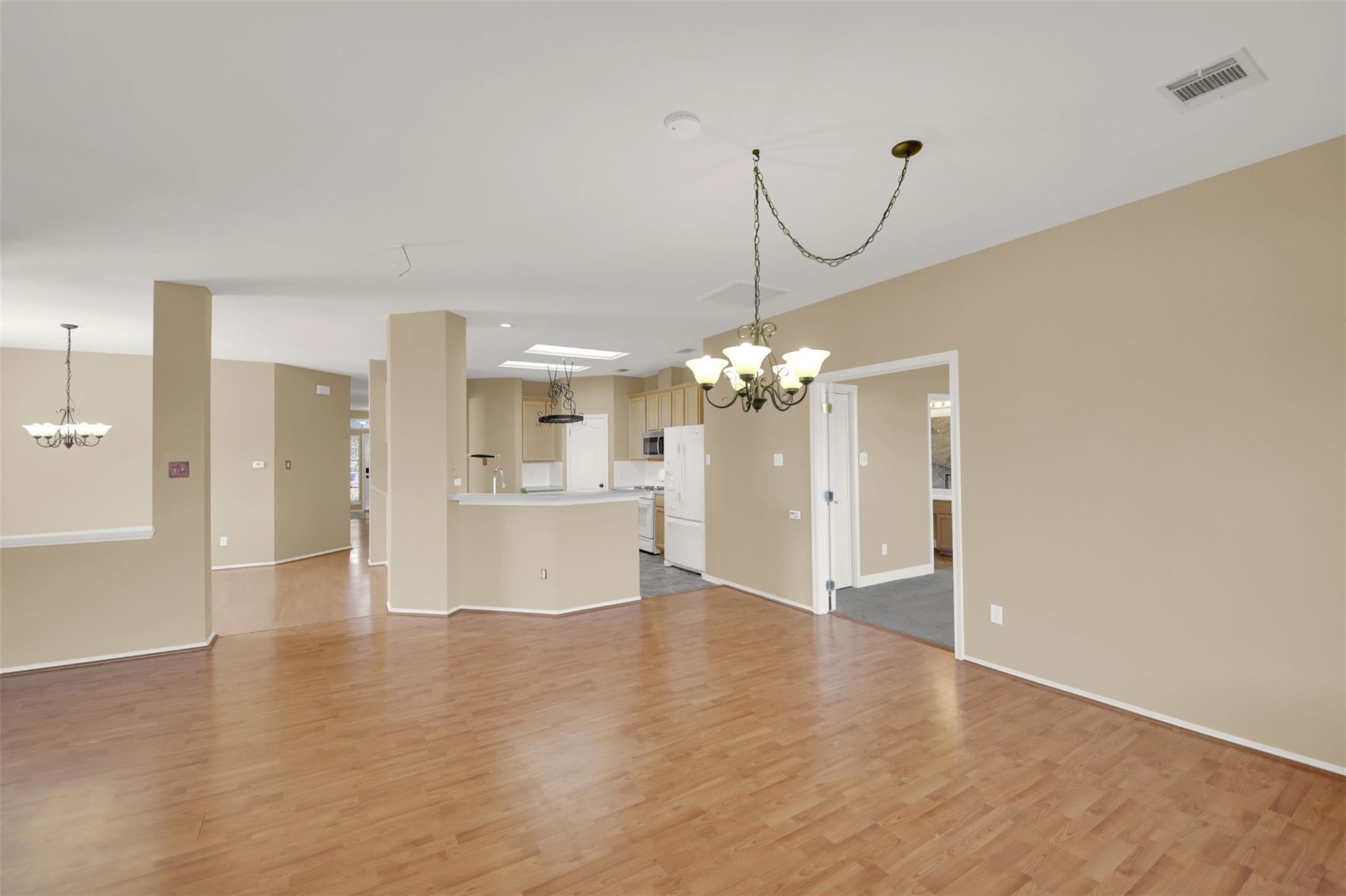 Open-plan living and dining area with wood floors, two chandeliers, and a kitchen breakfast bar.