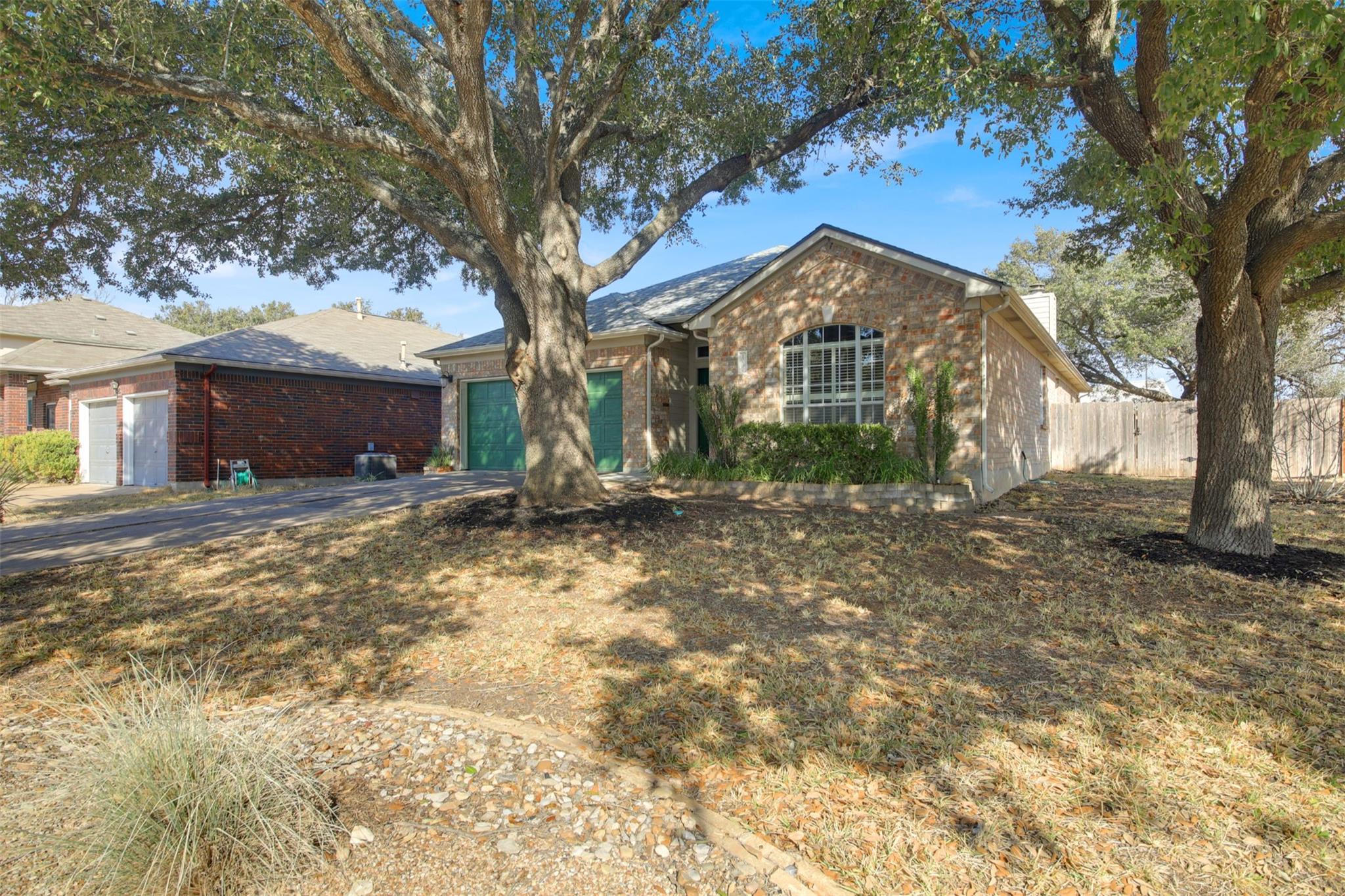 Brick house with green garage doors and an arched window, framed by large shade trees.