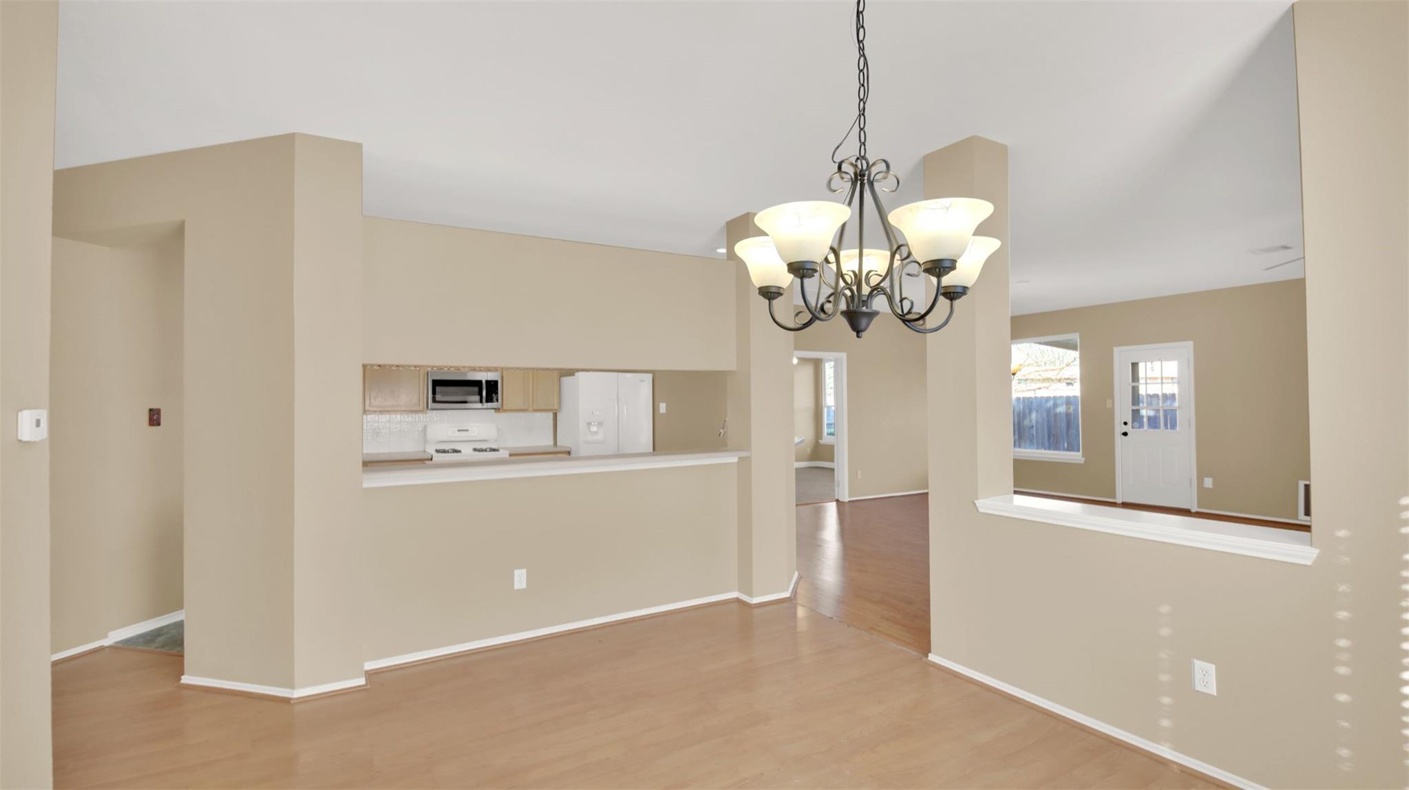 Open dining area with a chandelier, wood flooring, and a pass-through to the kitchen.