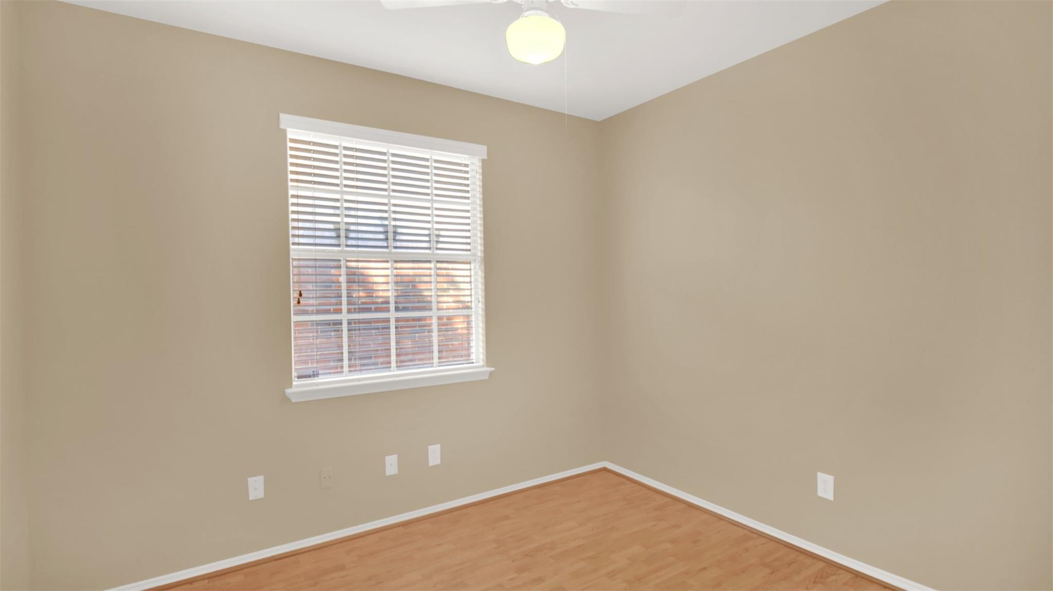 Empty room with beige walls, light wood flooring, and a window with white blinds.