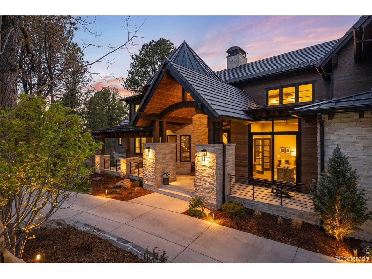 Modern home with a peaked metal roof and warmly lit windows at dusk.