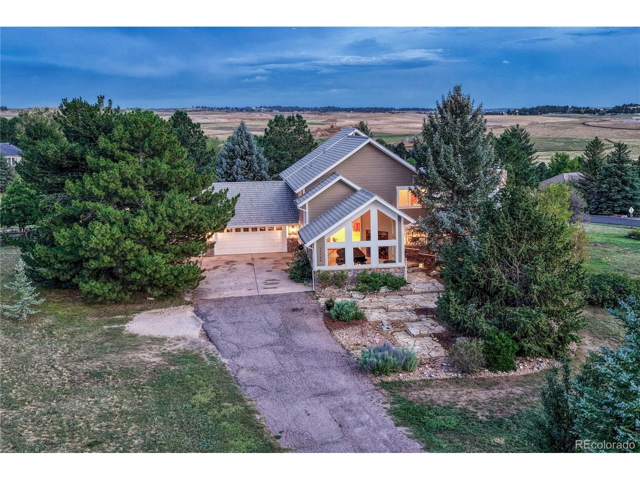 Aerial view of a two-story home with a broad driveway, stone walkway, and mature evergreens.