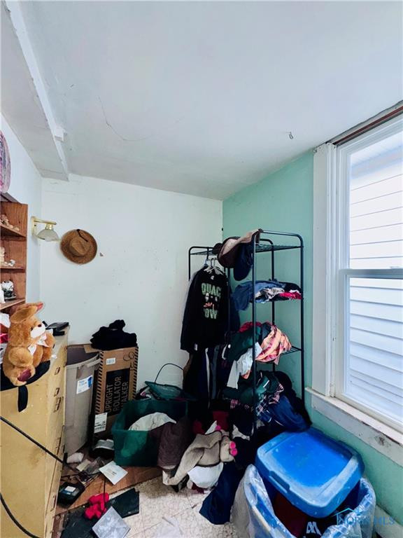 Cluttered room with a clothing rack, scattered belongings, and a large window.