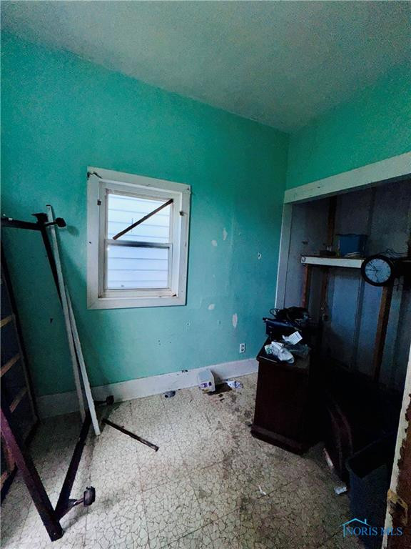 Worn room with turquoise walls, a small window, open closet, and cracked flooring.