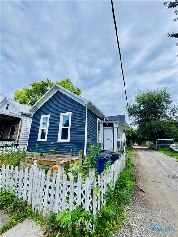 Blue-sided house with white trim behind a white picket fence, beside a gravel driveway.