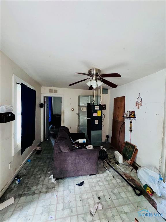 Living room with a purple sofa, ceiling fan, and cluttered patterned tile floor.