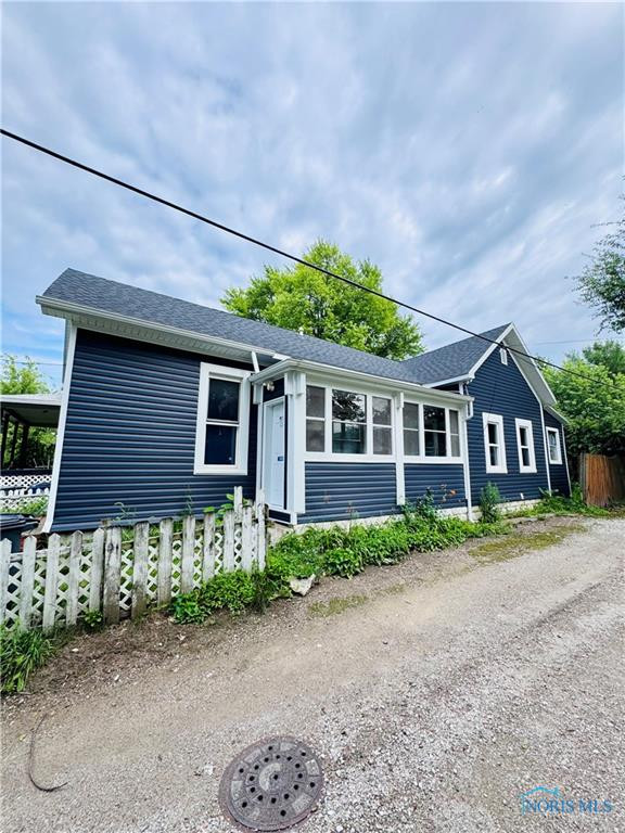 Dark blue house with white trim, an enclosed sunroom, and a gravel driveway.