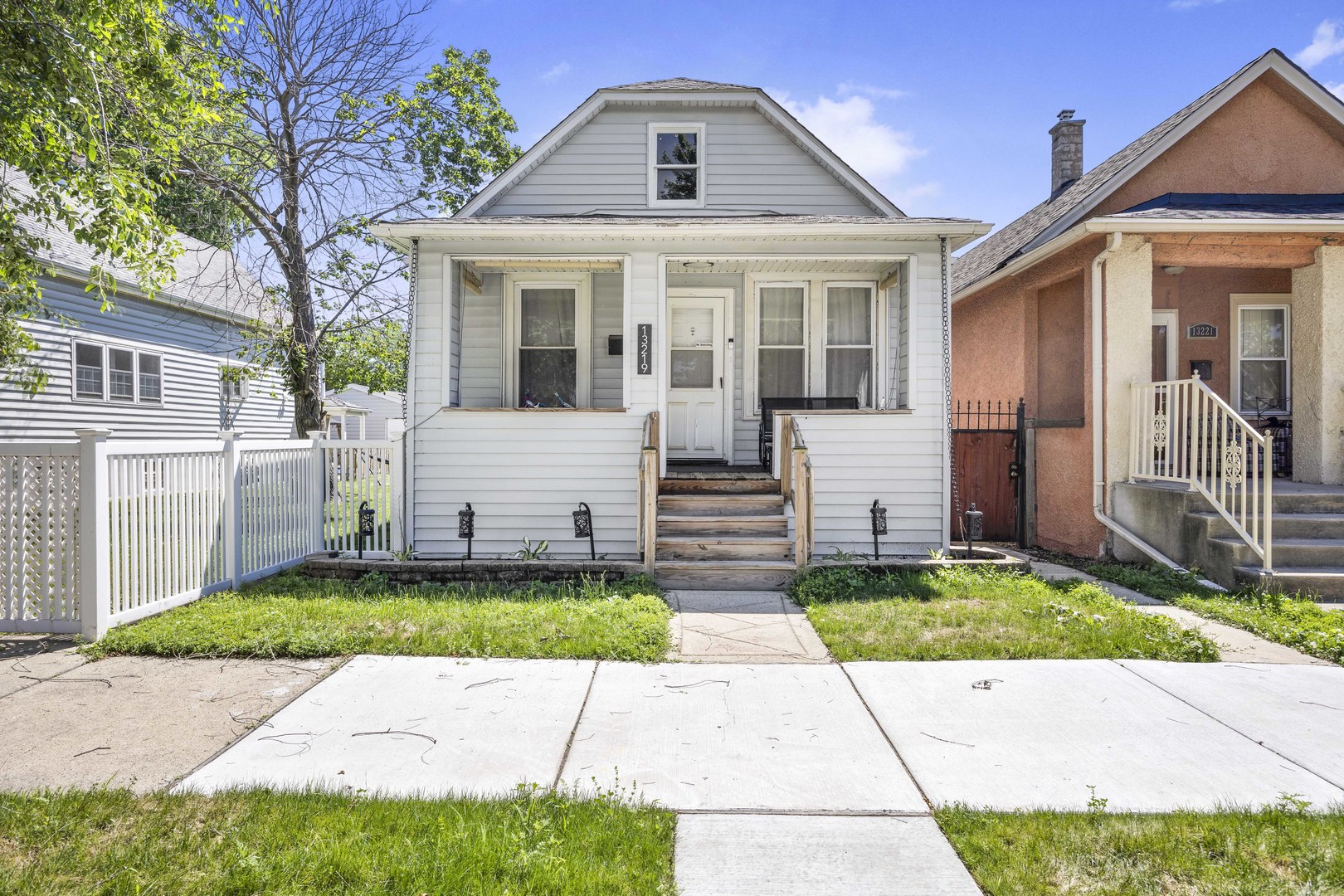 White-sided house with a covered porch and central wooden steps, between two neighboring homes.