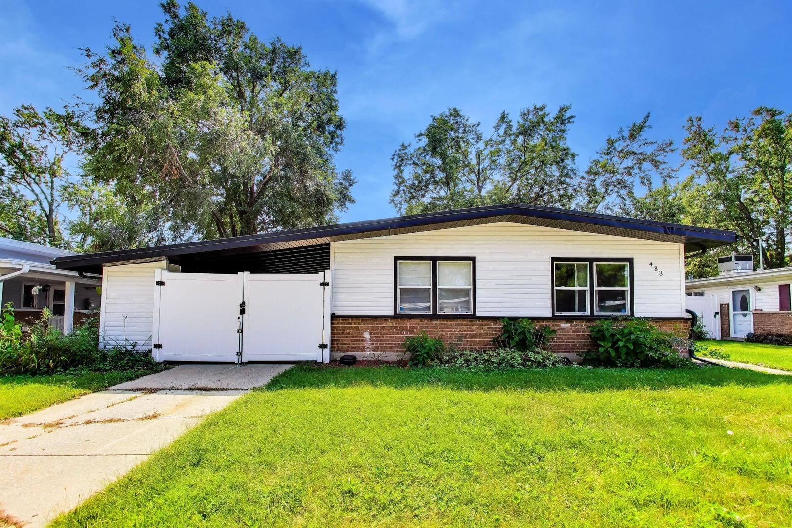 Single-story white-sided home with brick facade, dark low roof, white driveway gate, and green lawn.