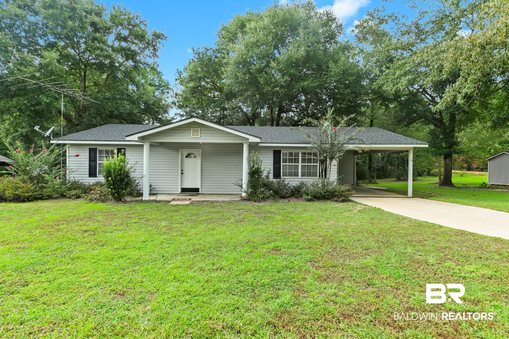 Single-story gray house with a covered entry and carport on a tree-lined lawn.