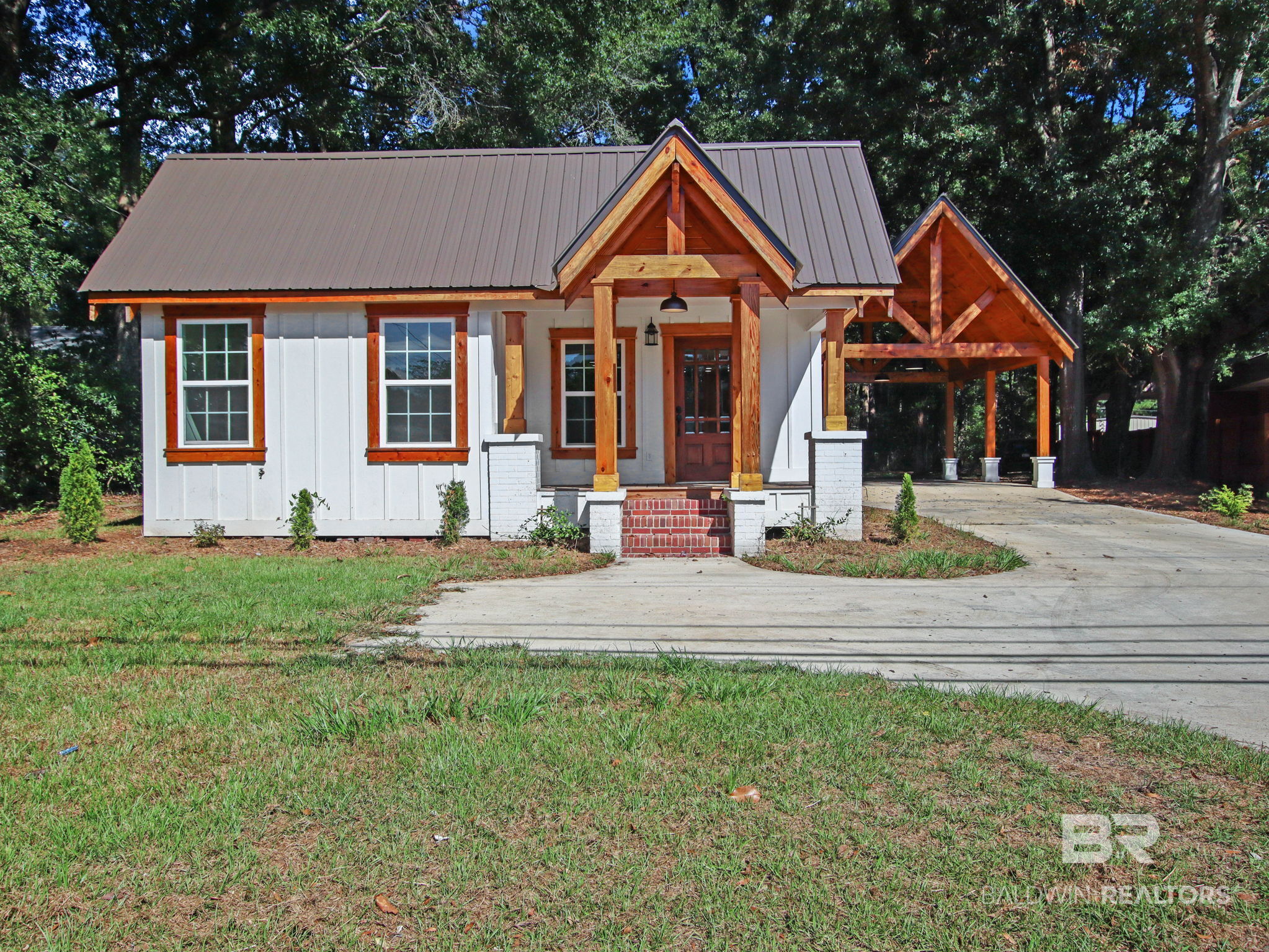 White house with timber gabled porch, red brick steps, and attached carport beneath a dark metal roof.