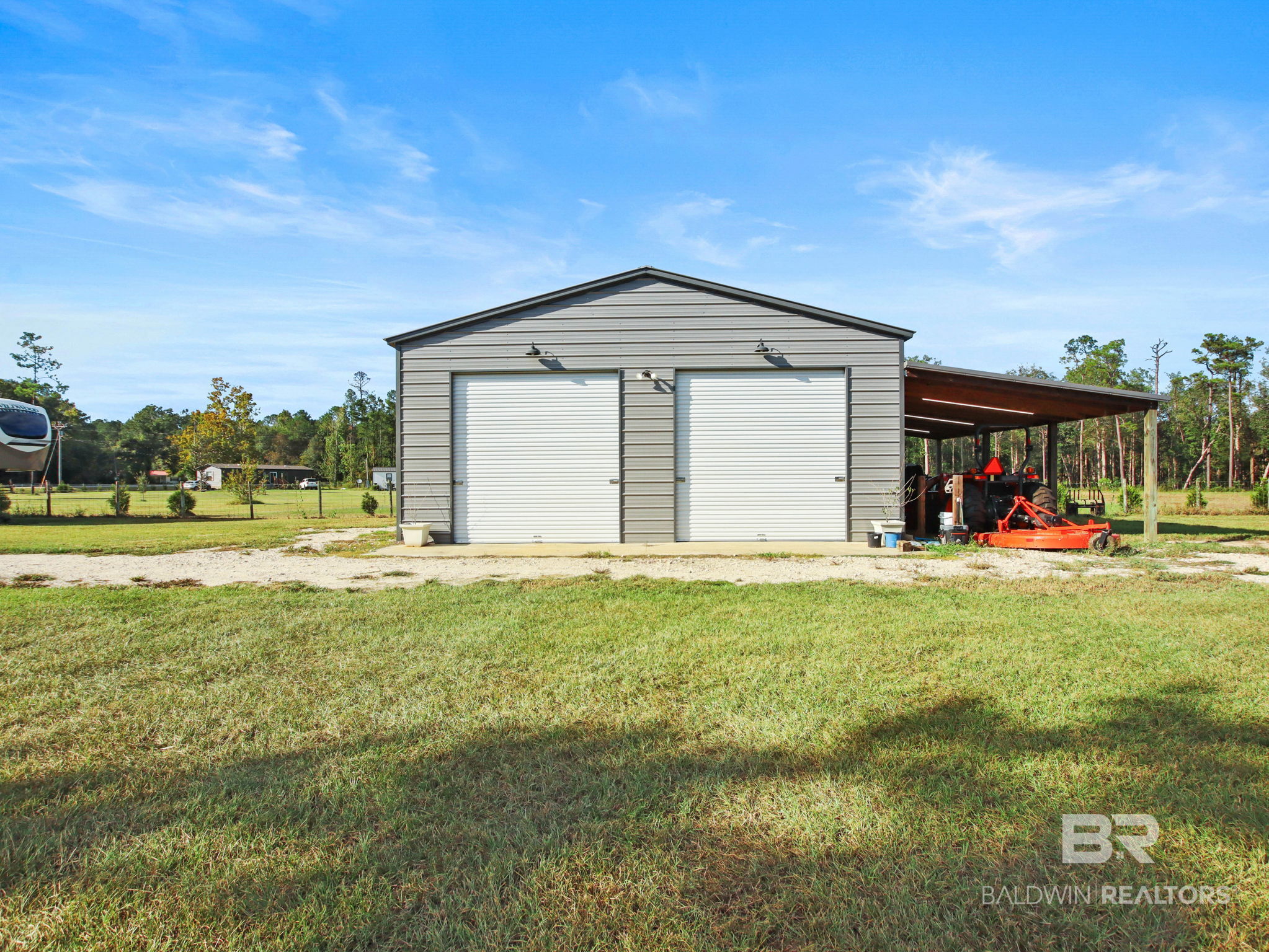 Gray metal outbuilding with two roll-up doors and a carport sheltering a tractor.