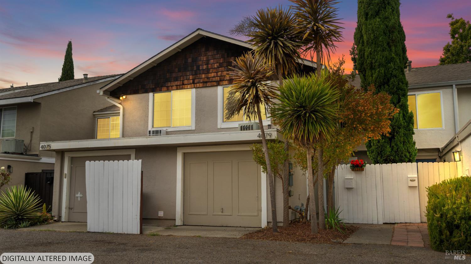Attached homes with garage doors and white fences beneath a pink dusk sky.