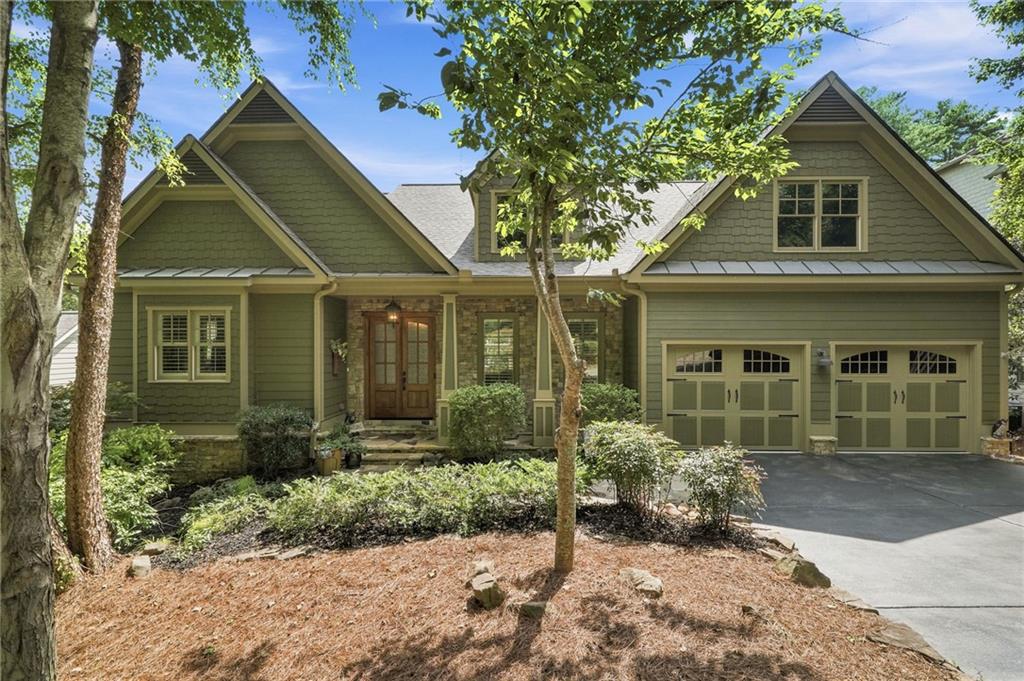 Green gabled home with stone accents, a double garage, and mature trees in the front yard.