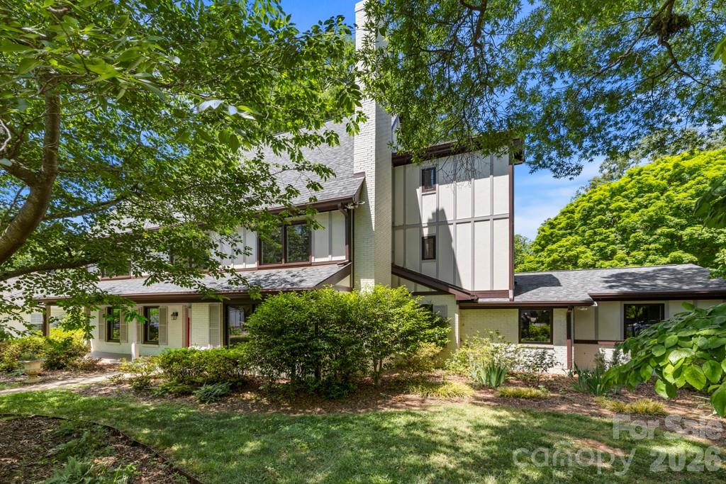 Multi-level white house framed by mature trees, with a landscaped lawn and shrubs.