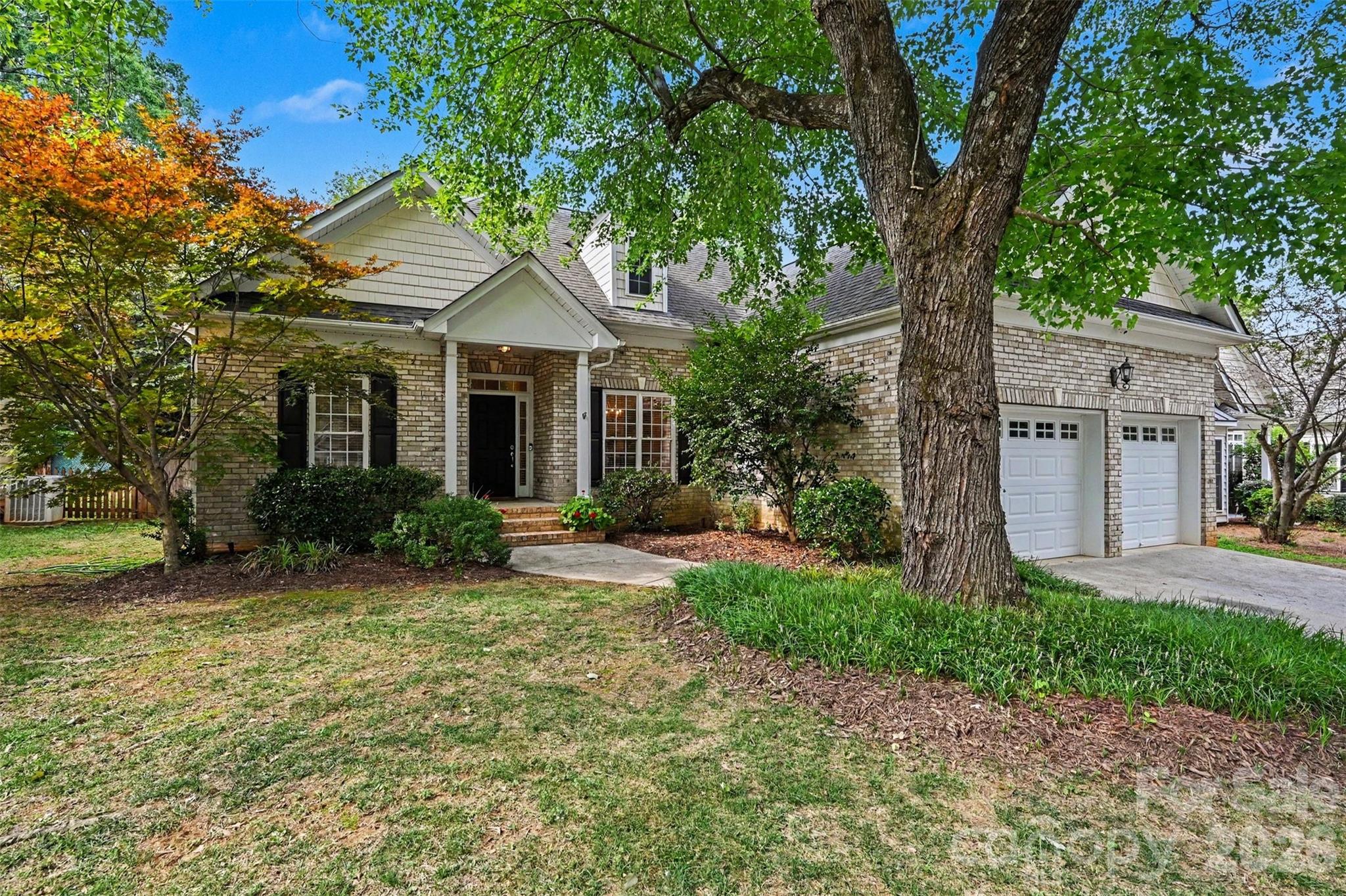 Brick house with a covered entry and double garage behind a large mature tree.