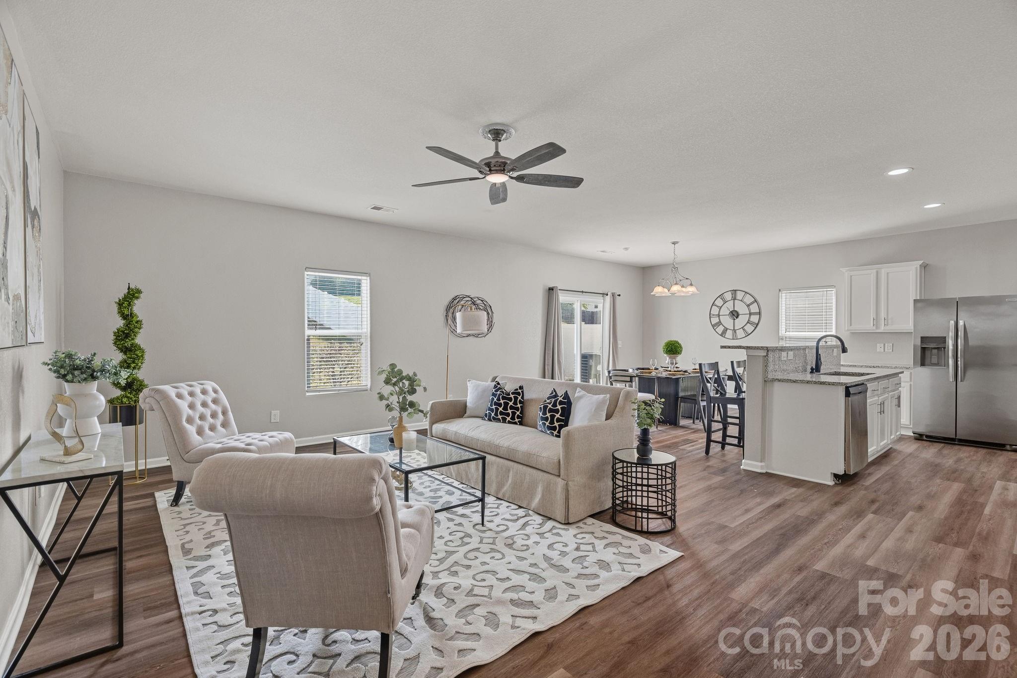 Staged open-plan living room and kitchen with a granite island and stainless steel appliances.