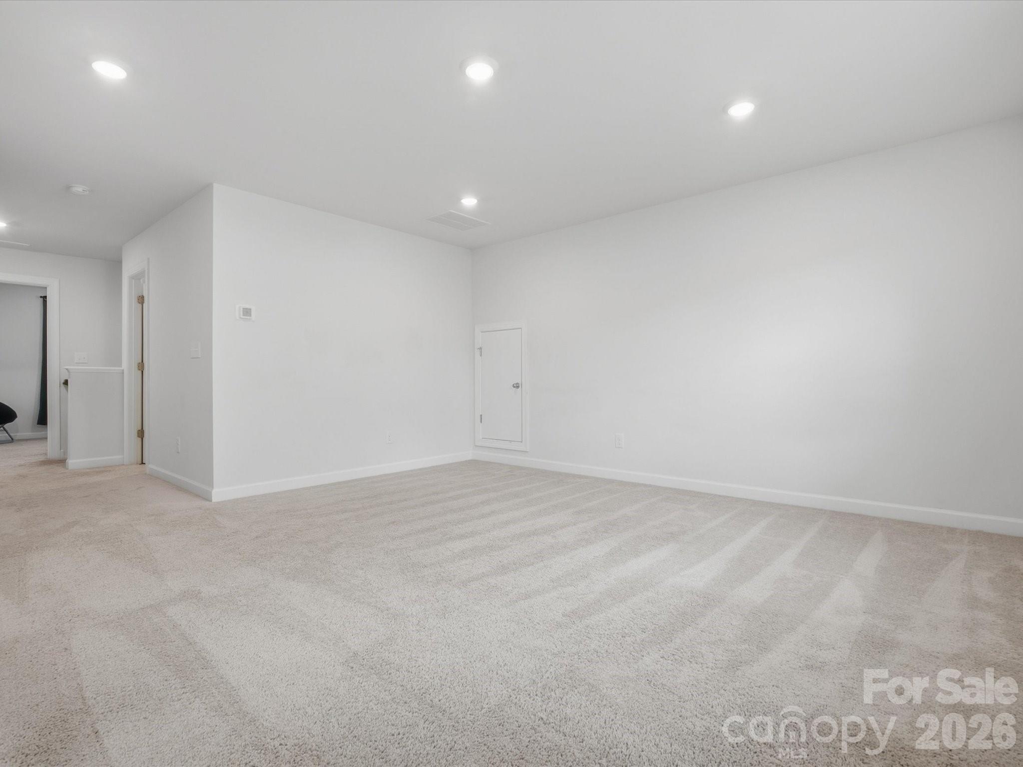 Empty carpeted room with white walls, recessed lights, and a small access door.