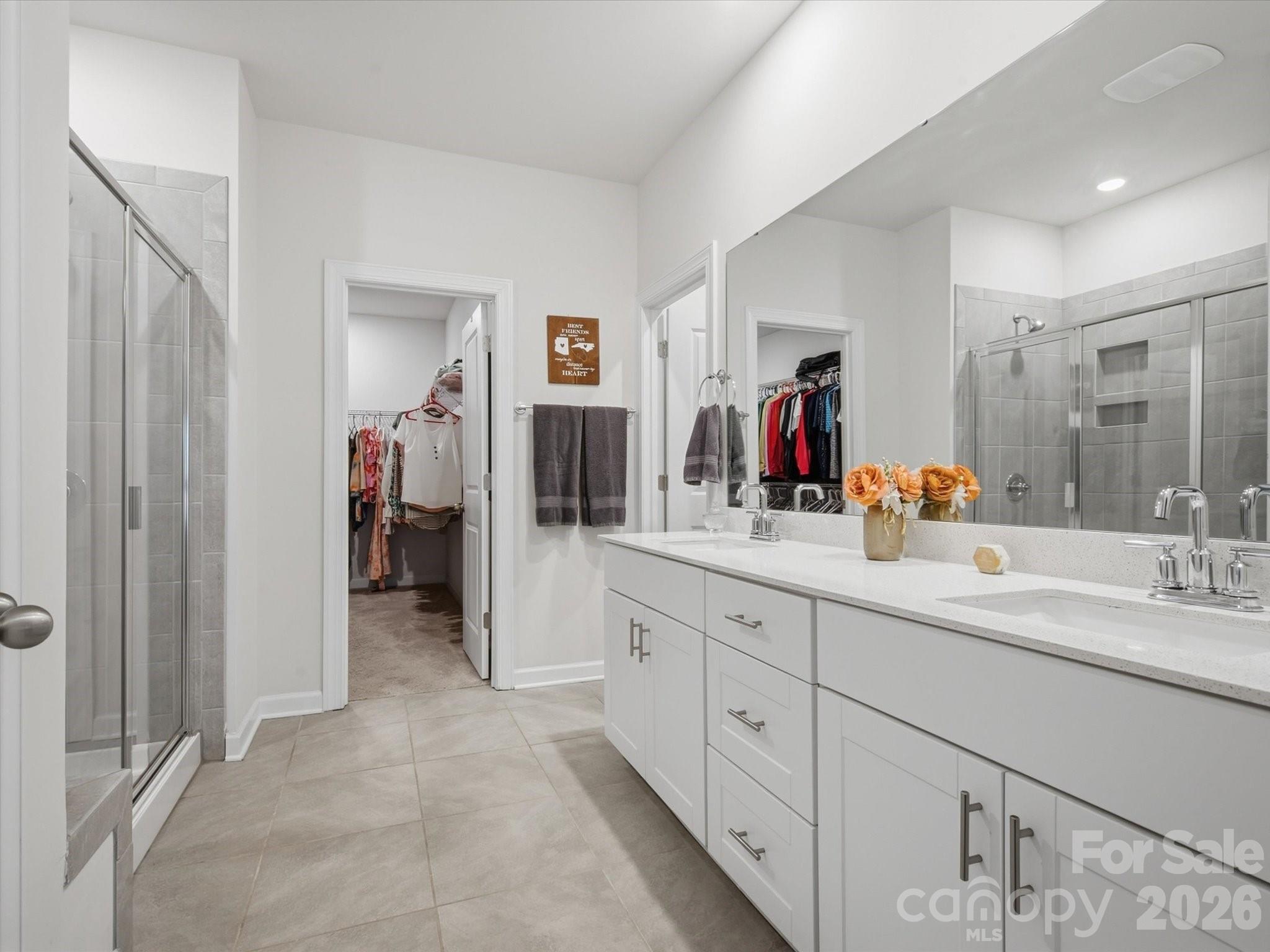 Primary bathroom with a long white double vanity, tiled glass shower, and open closet.