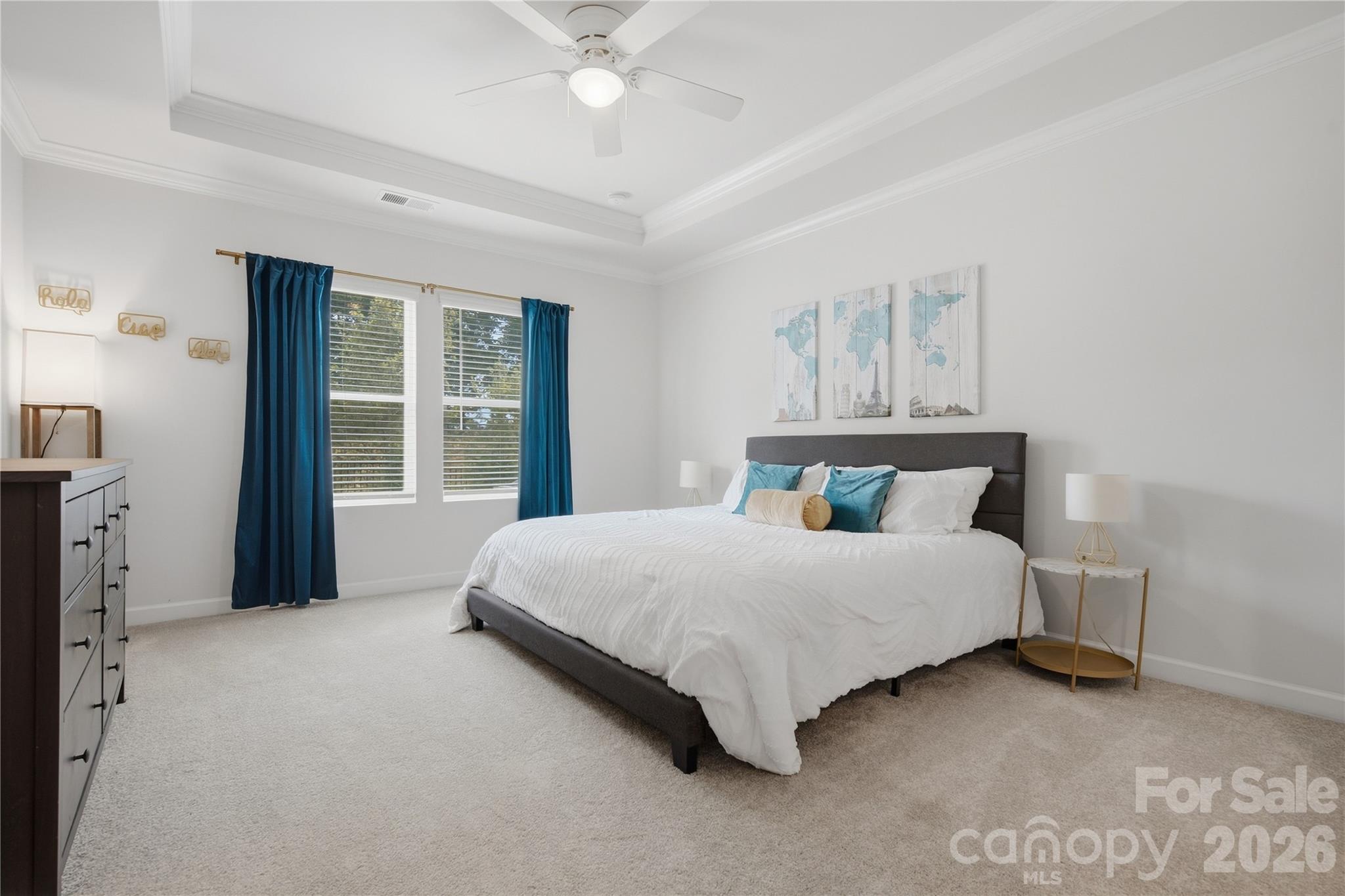 Staged bedroom with a white bed, teal curtains and pillows, and map prints above the headboard.