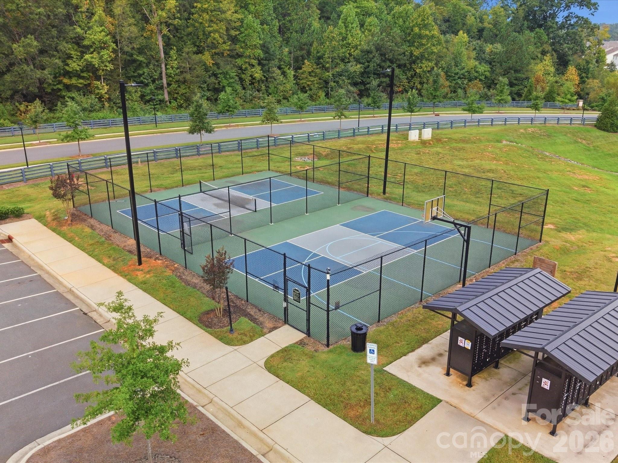 Fenced community courts with a basketball hoop, a second marked court, and covered parking nearby.