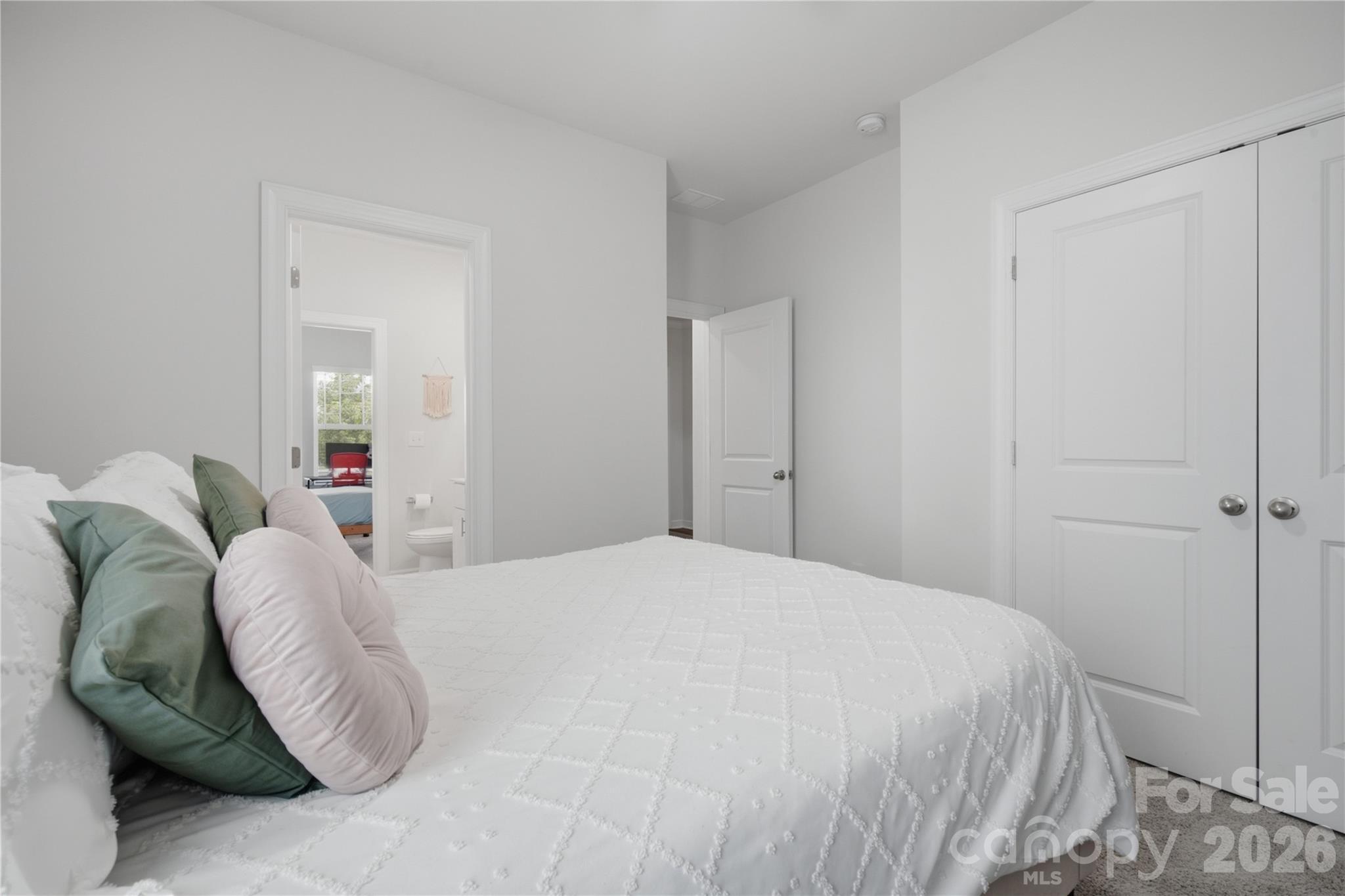 Bedroom with a white quilted bed, colorful pillows, and double closet doors.
