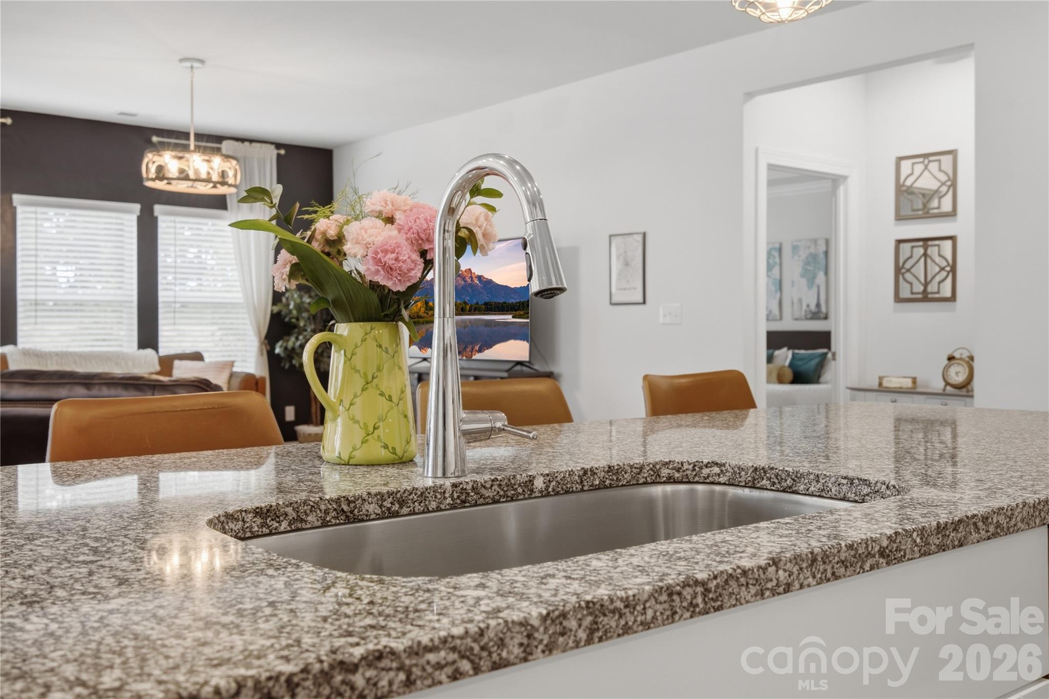 Kitchen with a granite island, undermount sink, tall chrome faucet, and pink flowers.
