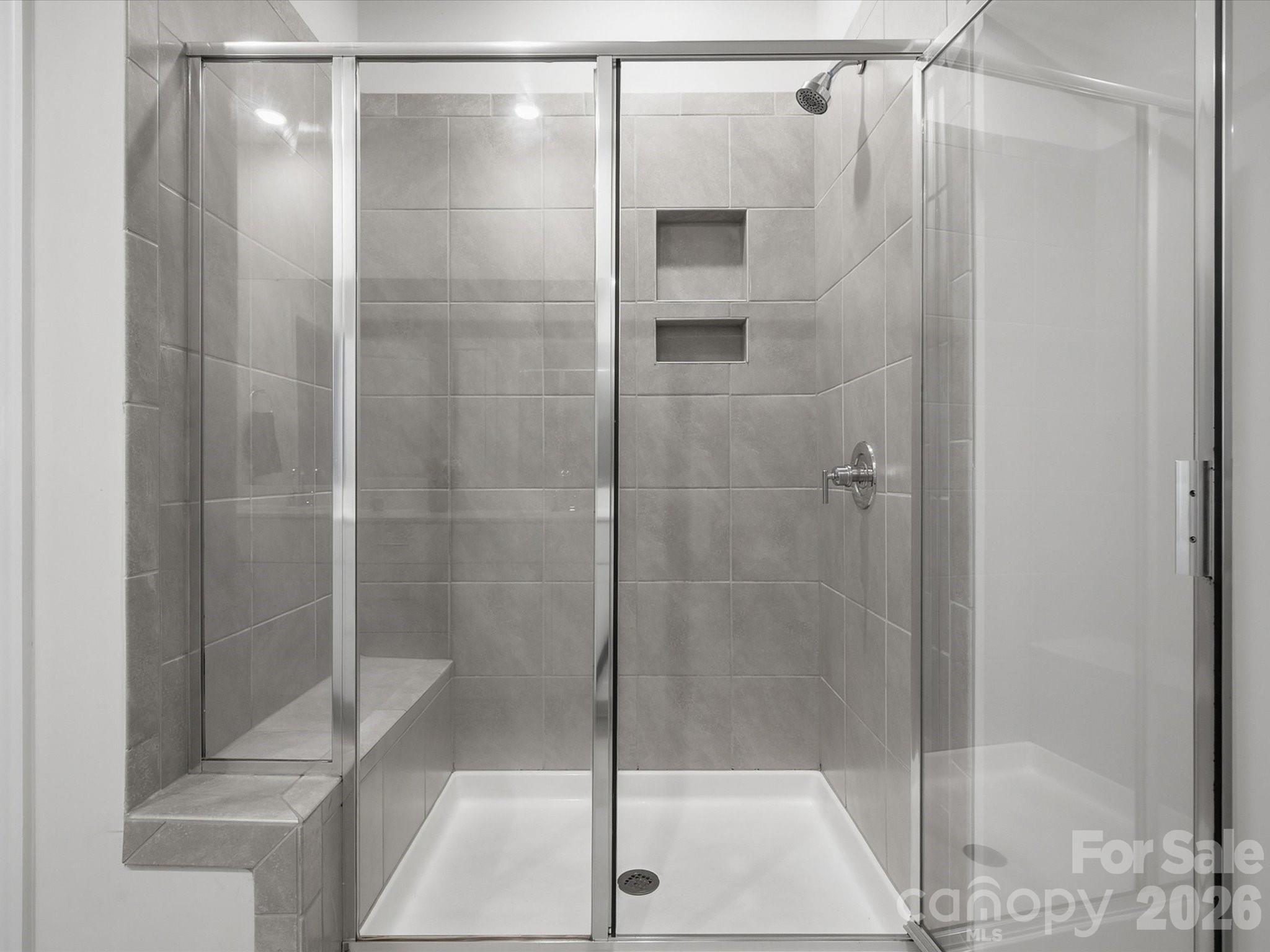 Walk-in shower with gray tile, clear glass doors, built-in bench, and recessed niches.