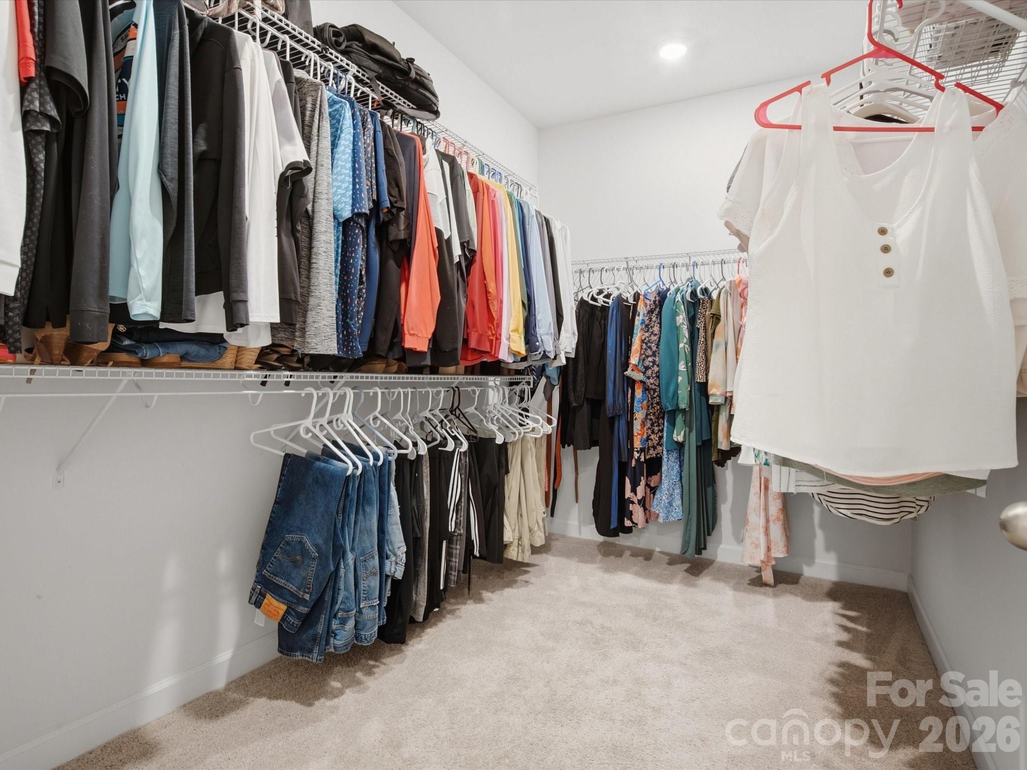 Walk-in closet with clothing on white wire racks and a white sleeveless top hanging in the foreground.