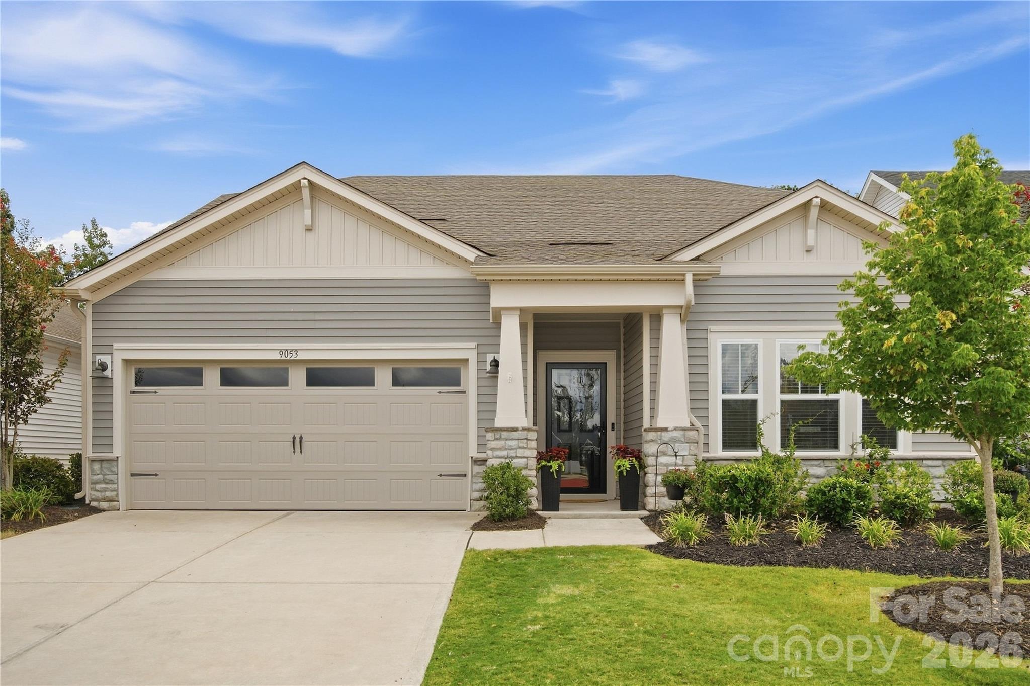 Single-story gray house with a two-car garage, covered entry, and landscaped front yard.