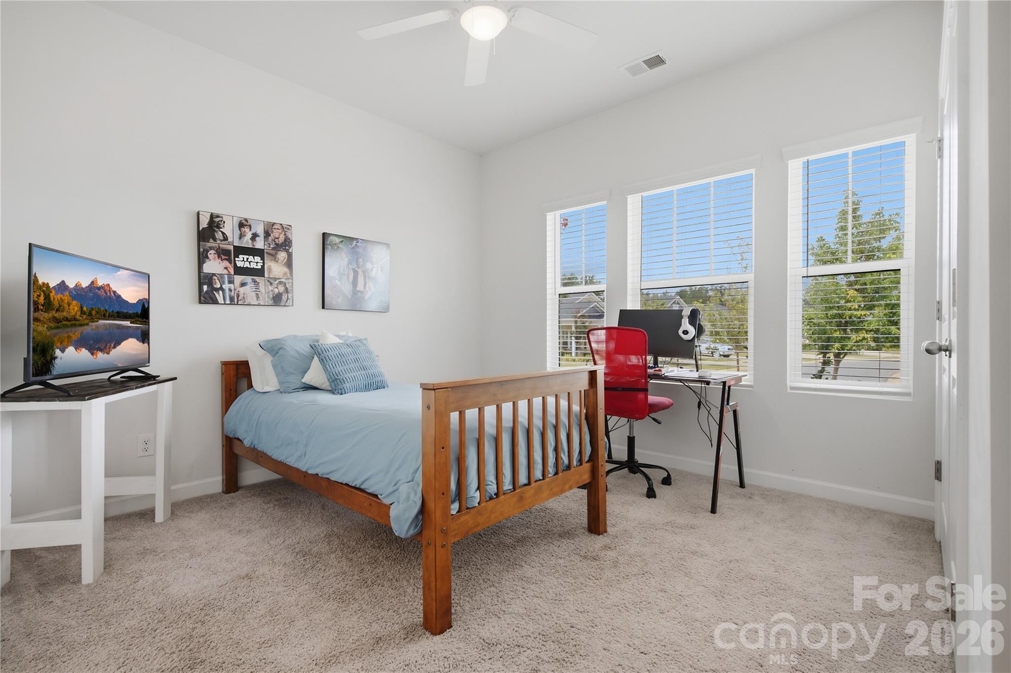 Bedroom with a wooden bed, pale blue bedding, and a desk beside three bright windows.
