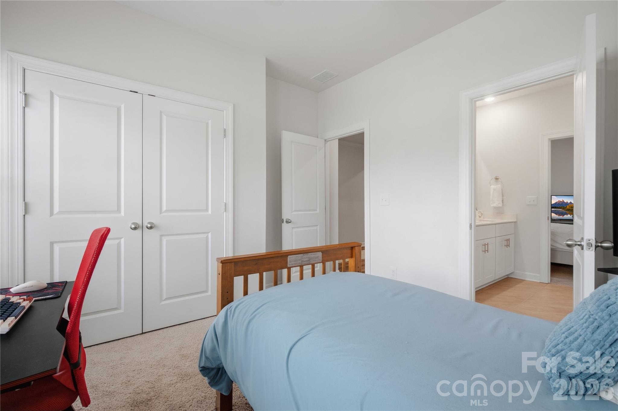 Bedroom with a blue-covered bed, wooden headboard, red desk chair, and open doorway to a bathroom.