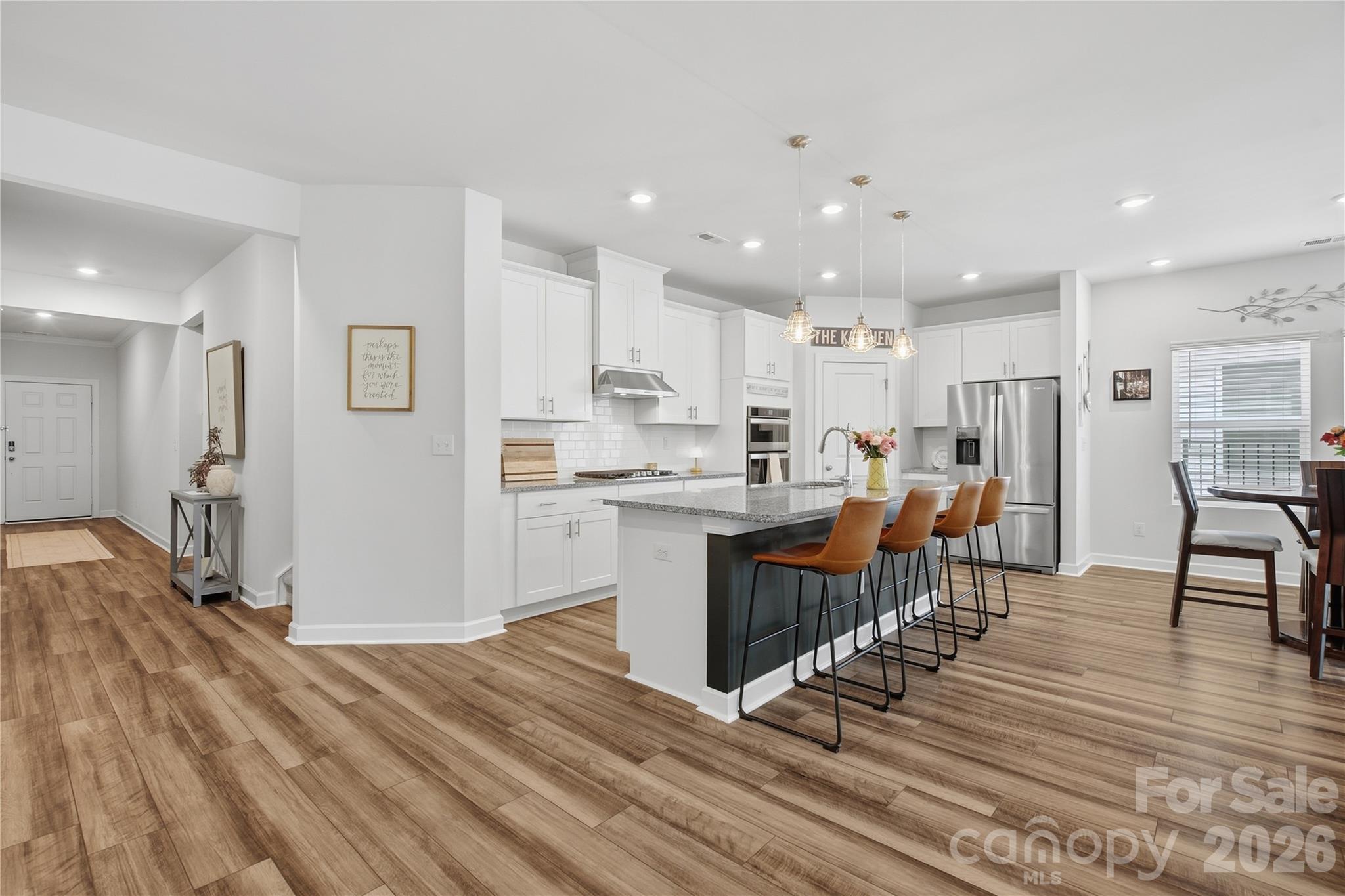 Bright kitchen with white cabinets, granite island, four bar stools, and adjoining dining area.
